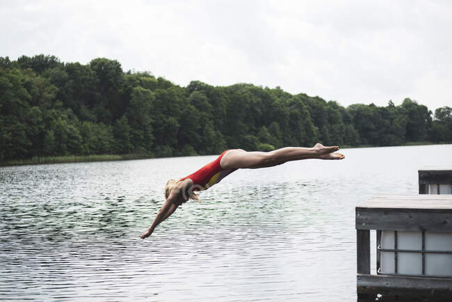 Athletic woman in red swimsuit diving into lake in Poland — Stock Photo