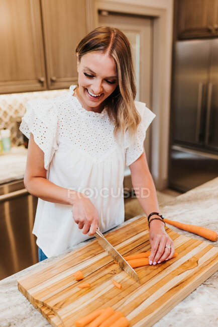 Jovem mulher cortando cenouras em casa — Fotografia de Stock
