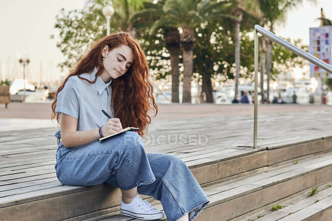 Jeune rousse femme écrit dans un petit carnet à l'extérieur — Photo de stock
