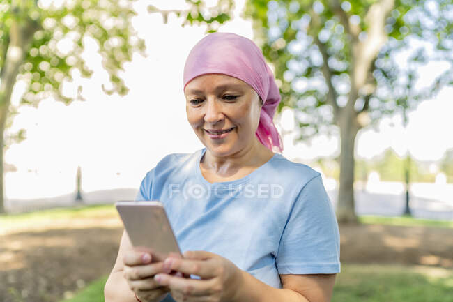 Femme avec écharpe de cancer en utilisant son smartphone — Photo de stock
