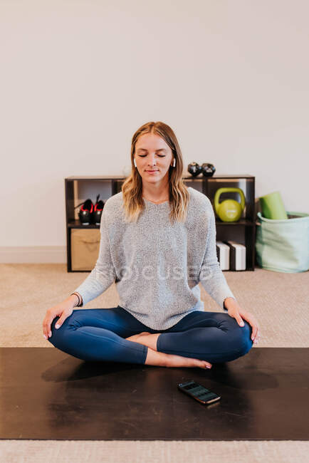 Hermosa joven sentada en el suelo y meditando en la esterilla de yoga - foto de stock
