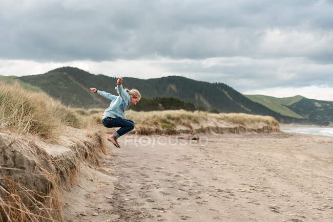 Preteen jumping on beach in New Zealand with mountains in background — Stock Photo
