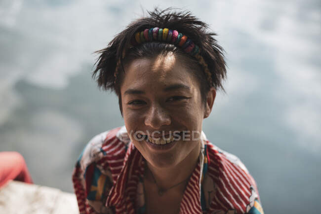 Non-binary asian person smiles in colourful shirt by lake — Stock Photo