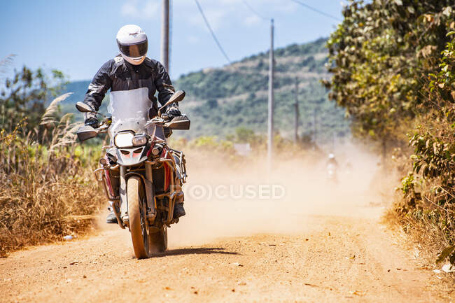 Человек на своем мотоцикле по пыльной дороге в Камбодже — стоковое фото