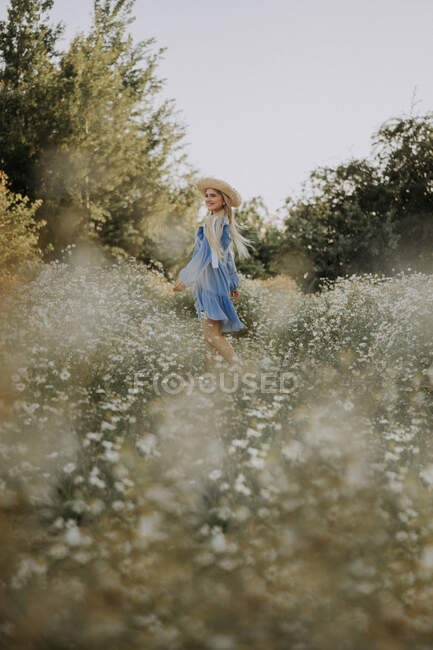 Eine junge Frau mit Strohhut steht in einem Kamillenfeld — Stockfoto