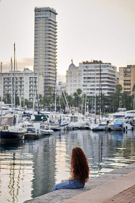Jovem ruiva mulher sentada olha para um porto de uma cidade — Fotografia de Stock