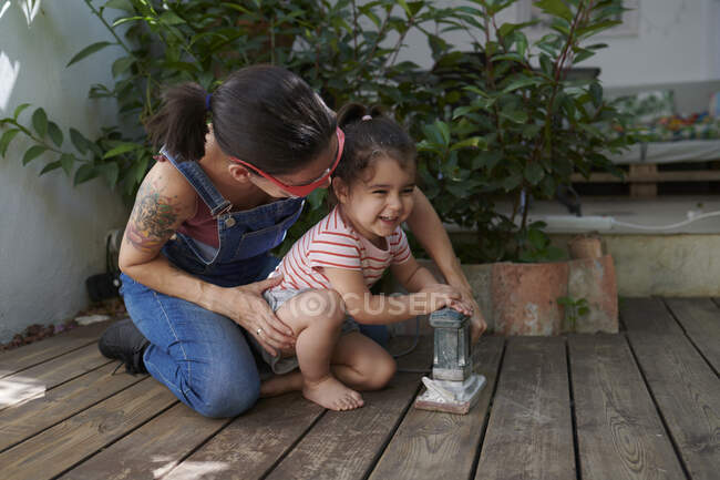 Madre e hija lijando la madera en el jardín - foto de stock