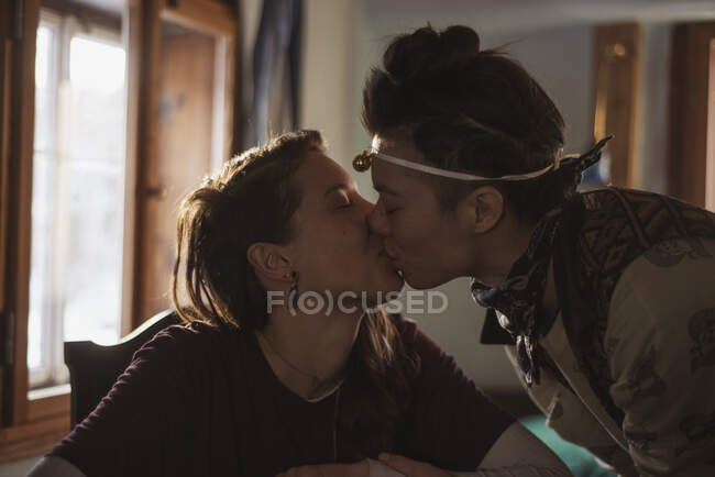 Queer female couple smile and kiss over gifts in cottage window — Stock Photo