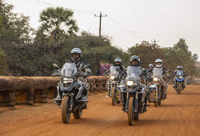 Група чоловіків їде на своєму пригодницькому мотоциклі по брудній дорозі в Камбоджі. — стокове фото