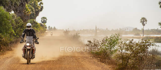 Homem montando sua moto de aventura na estrada empoeirada no Camboja — Fotografia de Stock