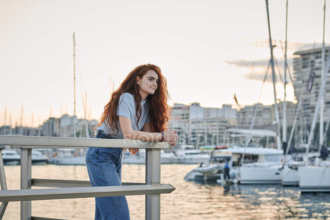 Mulher ruiva jovem olha para o mar em um porto de uma cidade — Fotografia de Stock