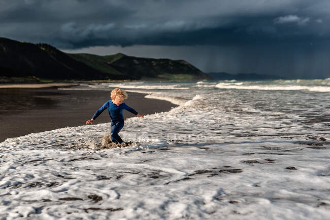 Щаслива дитина грає на пляжі з драматичним небом на фоні — стокове фото