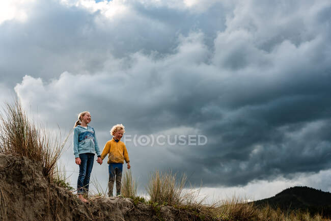 Children holding hands on sand dune with dramatic clouds in background — Stock Photo