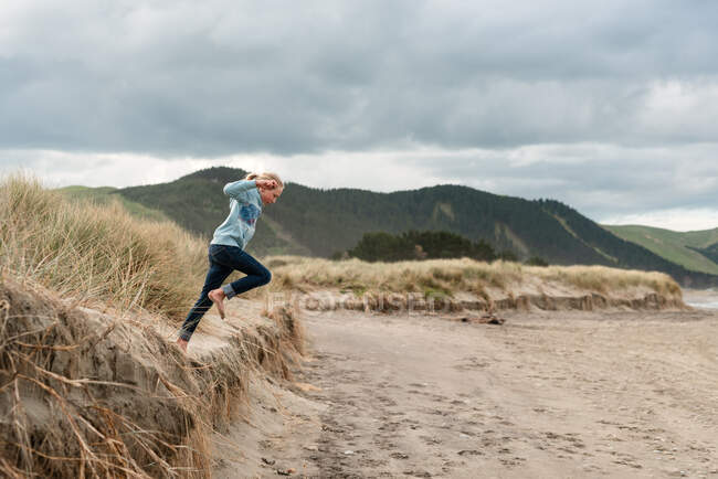 Girl leaping from sand dune at beach in New Zealand — Stock Photo