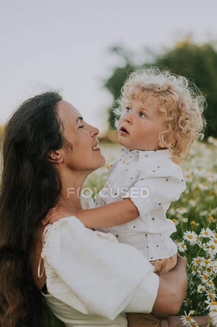 Una mujer sostiene a un niño pequeño en sus brazos en un campo. - foto de stock