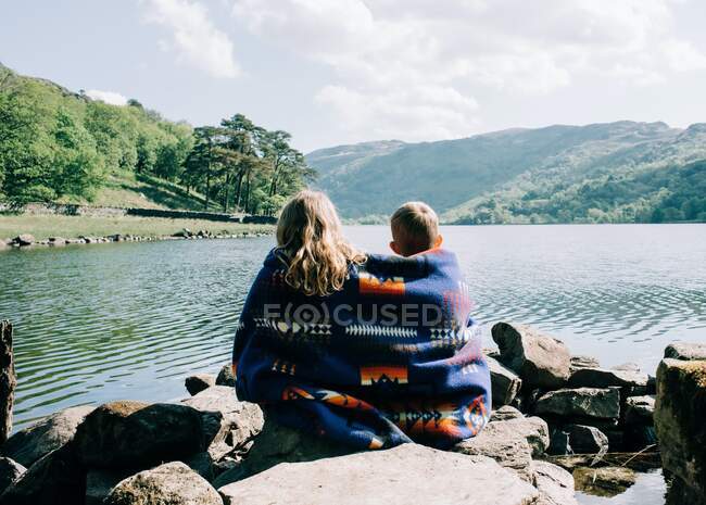 Kids sat wrapped up in Pendleton over looking a mountain and lake view — Stock Photo