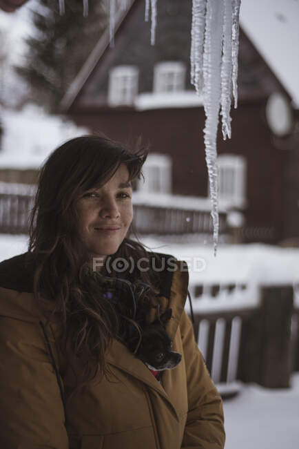Girl with small dog in jacket smiles under large icicles in Czech town — Stock Photo