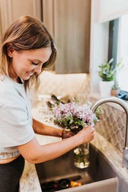 Beautiful young woman with flowers in the kitchen — Stock Photo