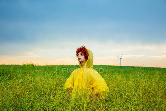 Young redhead guy in yellow raincoat on green rapeseed field — Stock Photo