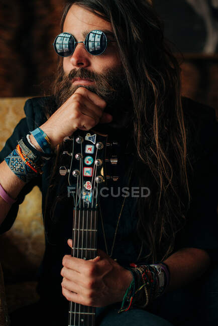 Portrait d'un musicien en lunettes de soleil noires appuyé sur le cou d'une guitare avec une expression de visage coûteuse — Photo de stock