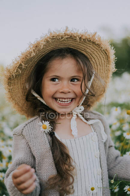 A girl in a hat, smiling against the background of a chamomile field. — Stock Photo