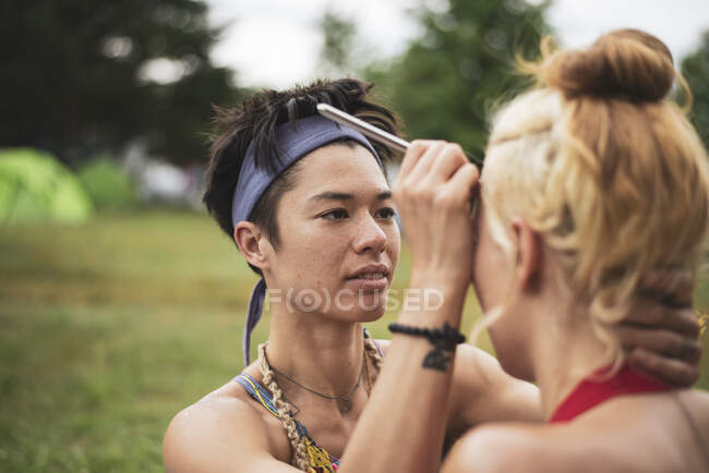 Mixed-race athletic woman paints friends face camping at festival — Stock Photo