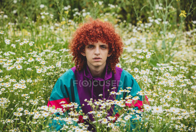 Young guy with red curly hair in 80s sports suit on chamomile meadow — Stock Photo