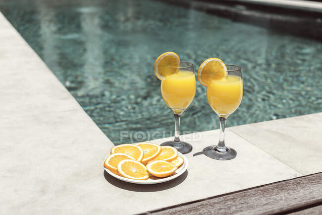 Освежающие апельсиновые коктейли в стаканах возле бассейна — стоковое фото