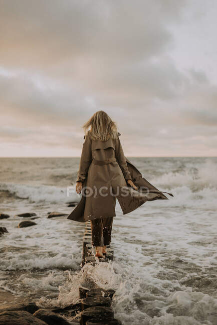 Girl in a trench coat walking along the breakwaters — Stock Photo