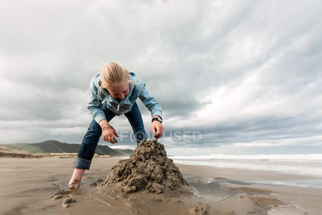 Tween building sand castle at beach in New Zealand on cloudy day — Stock Photo