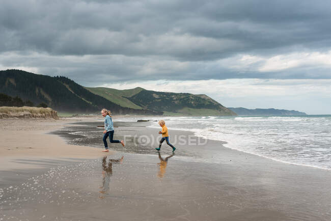 Двоє дітей біжать на прекрасному пляжі в похмурий день у Новій Зеландії. — стокове фото