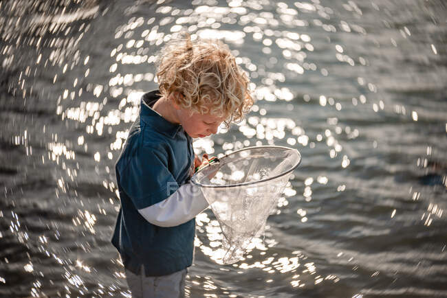 Neugieriges Kind schaut in Netz mit Wasser im Hintergrund — Stockfoto