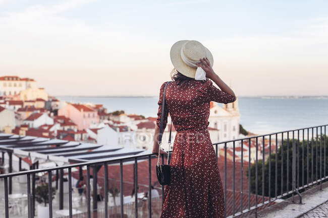 Mujer con sombrero de paja y vestido en un punto de vista en Lisboa, Alfama - foto de stock
