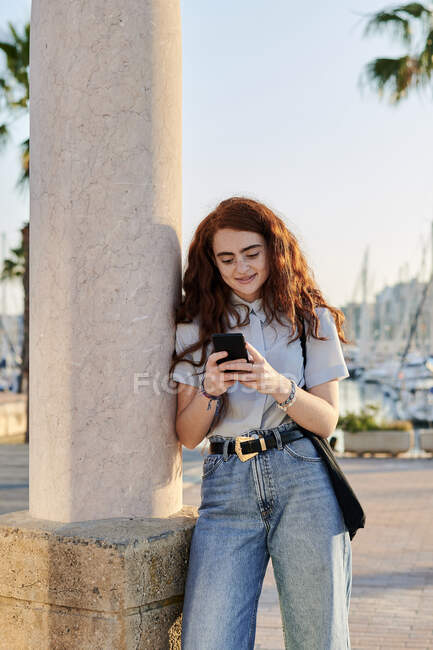 Giovane rossa donna guarda il suo cellulare in un porto marittimo — Foto stock