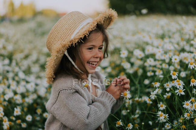 Kleines Mädchen mit Strohhut steht auf einem Gänseblümchenfeld — Stockfoto
