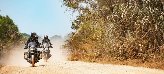 Hombres montando sus motos de aventura en carretera polvorienta en Camboya - foto de stock