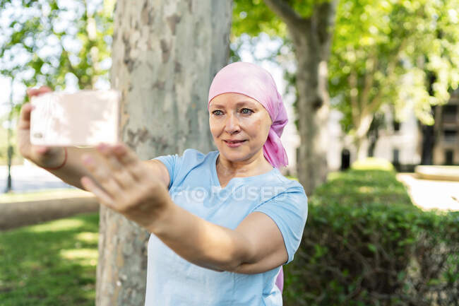 Щаслива жінка з раковим шарфом фотографує себе зі своїм смартфоном — стокове фото
