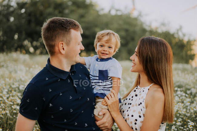 Uma família com uma criança está de pé, sorrindo, um campo — Fotografia de Stock