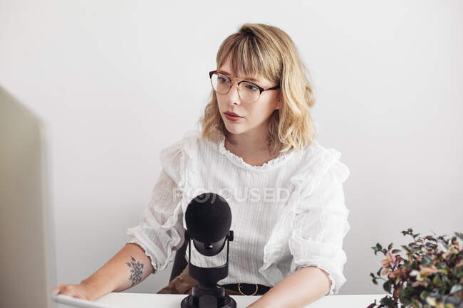 Блондинка в окулярах дивиться на комп'ютер. Мікрофон на столі — стокове фото