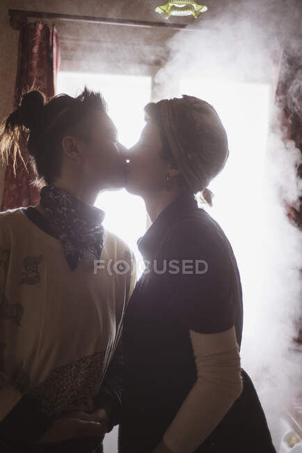 Queer female couple kiss in steamy kitchen cottage window in Czechnia — Stock Photo