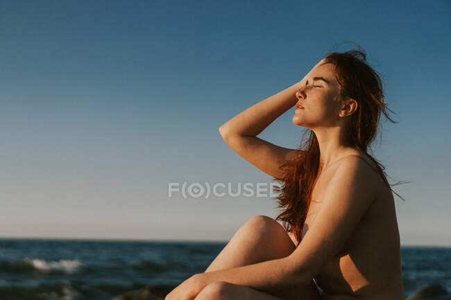 Giovane donna seduta nuda in riva al mare — Foto stock