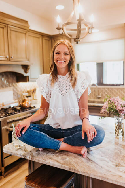 Porträt einer schönen jungen Frau in weißem Hemd und blauem Kleid, die auf einem Holztisch sitzt. — Stockfoto