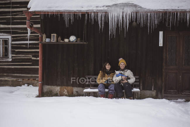 Queer female couple sit together in winter hut with icicles and dogs — Stock Photo