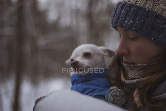 Hübsche Frau umarmt niedlichen Chihuahua in Jacke im winterlichen Schneewald — Stockfoto