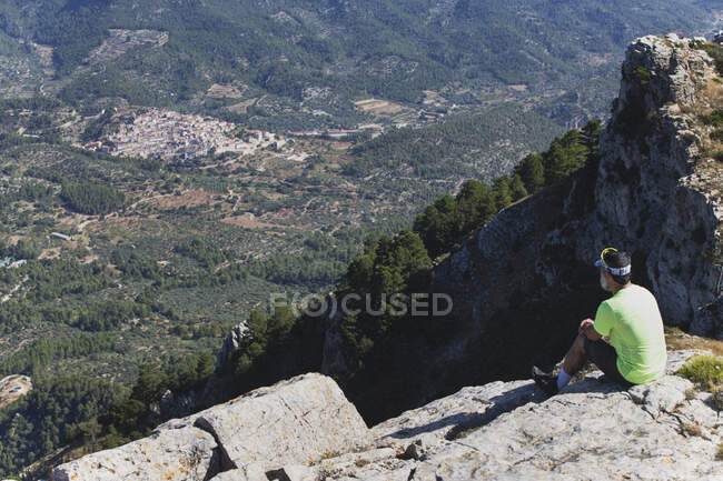Вид сбоку человека, сидящего на скале и смотрящего на горы — стоковое фото