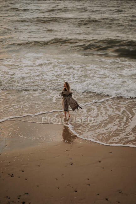 Girl with blonde hair in a trench coat walking by the sea — Stock Photo