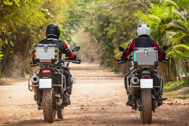 Двоє чоловіків їдуть на своєму пригодницькому мотоциклі по брудній дорозі в Камбоджі. — стокове фото
