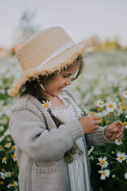 A little girl in a hat stands in a chamomile field. — Stock Photo