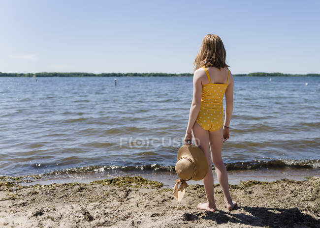 Tween menina em um maiô amarelo com chapéu de sol pela margem do lago. — Fotografia de Stock