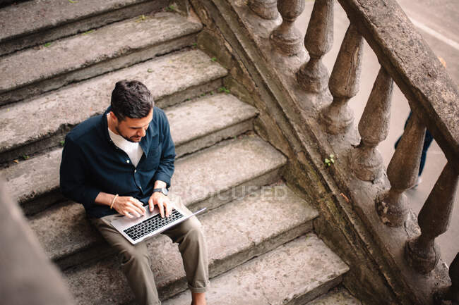 Человек с ноутбуком сидит на ступеньках в городе — стоковое фото